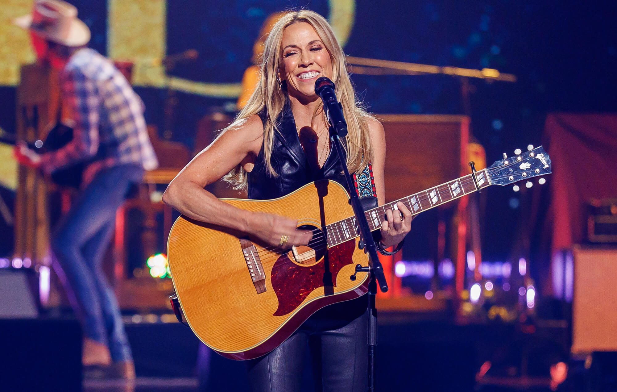Singer smiling at the microphone while playing an acoustic guitar on stage